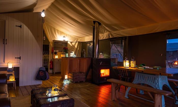 The lounge and dining area of the inside of Afon safari tent, with trunk coffee table, the fire light and dining table in the foreground